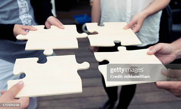 four people complete a large jigsaw puzzle - 4 piece puzzle stockfoto's en -beelden