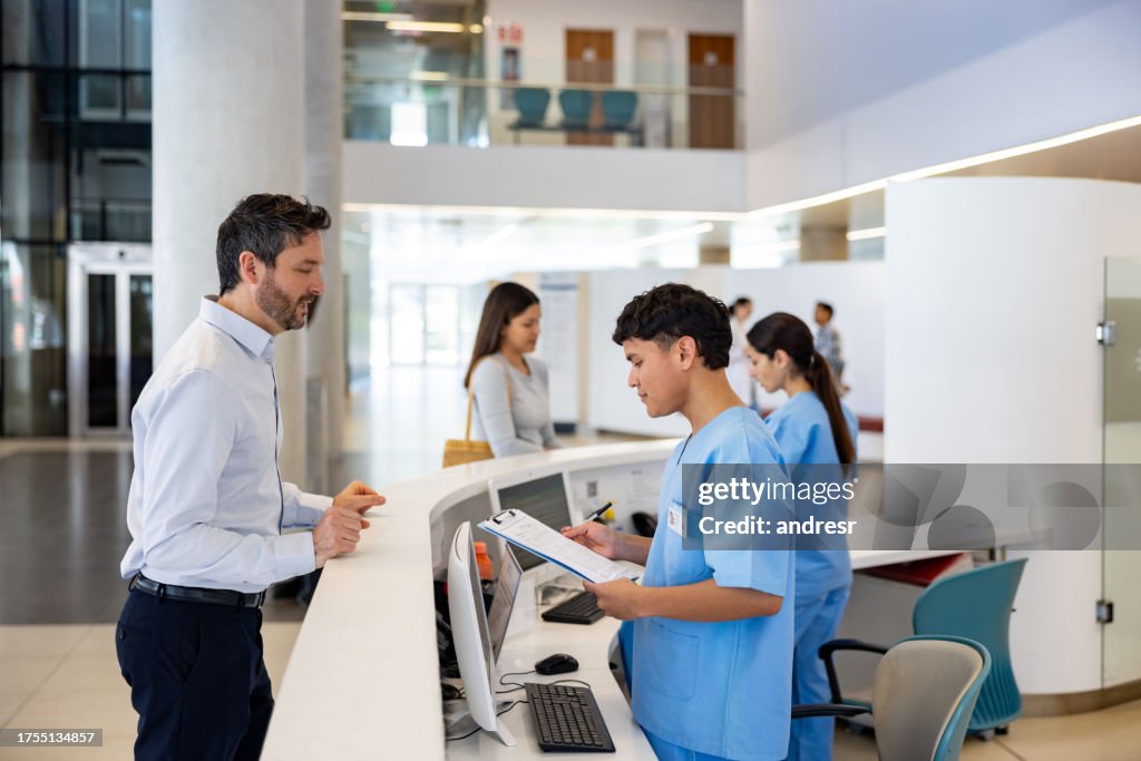 Mann kommt ins Krankenhaus und spricht mit einer Krankenschwester an der Rezeption
