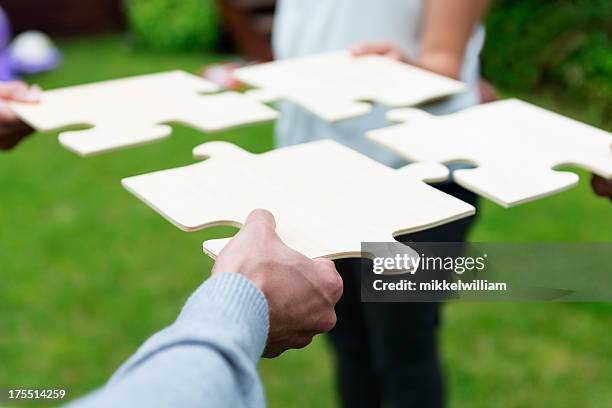 four individuals unite with giant puzzle pieces - big puzzle stock pictures, royalty-free photos & images