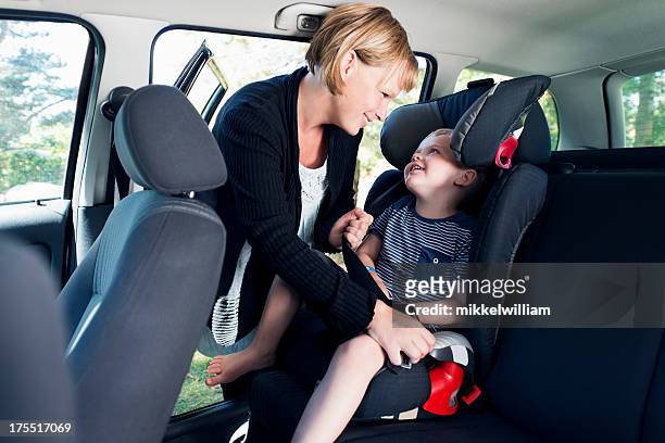 mother is securing child in a car with seat belt - soccer mom stock pictures, royalty-free photos & images