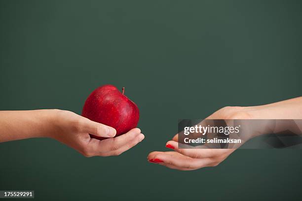 little student hand giving red apple to teacher before blackboard - appreciation stockfoto's en -beelden