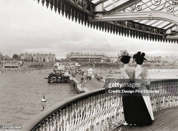 Two women look down on Clacton pier at Clacton-on-Sea, Essex, England towards the end of the 19th century. After a print by an unknown photographer.