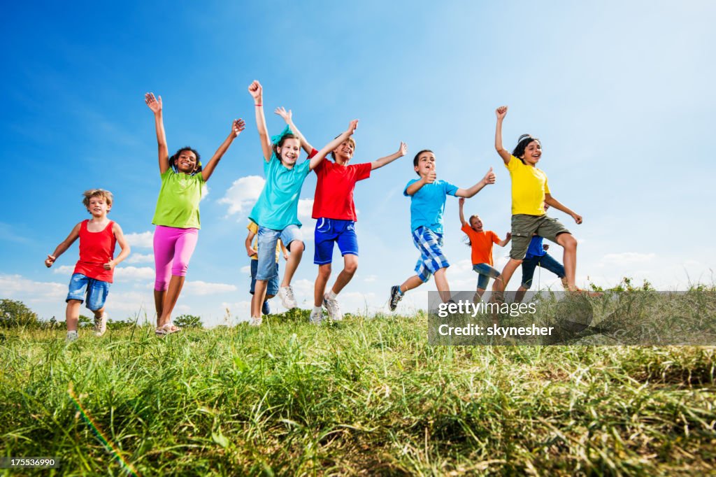 Happy kids with raised arms running against the sky.