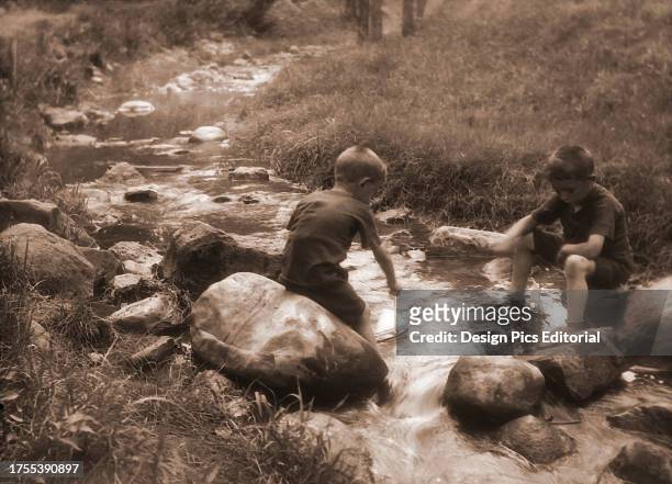 Two young boys playing with model boats in a stream circa 1900; England.