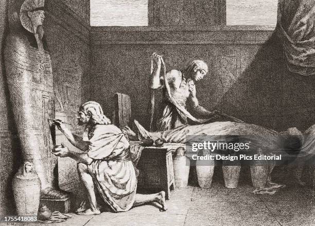 Ancient Egyptian funerary workers prepare a body for mummification. The worker on the right, the embalmer, is beginning to wrap the artificially...