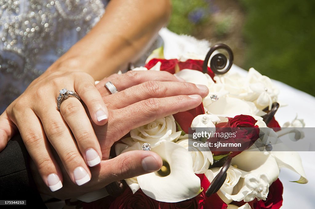 Braut und Bräutigam halten Hände und Ringe auf Blumen-Strauß