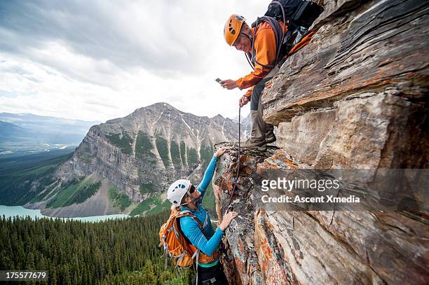 climber takes picture of teammate ascending cliff - woman climbing rope stock-fotos und bilder
