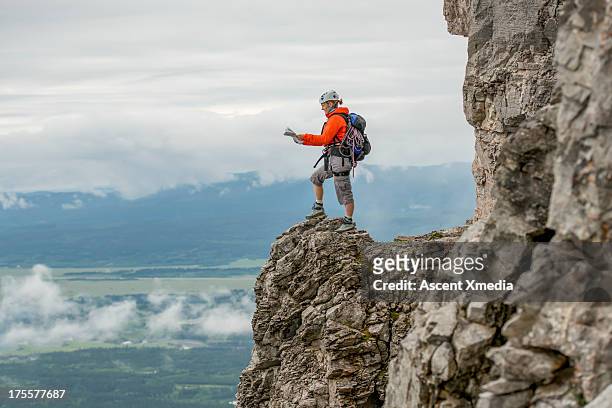 climber checks map, on rock crest above valley - bergsteiger mit karte und rucksack stock-fotos und bilder