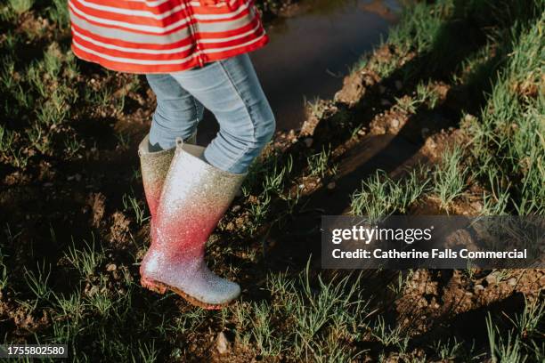 close-up of a child wearing glittery wellington boots and squelching through thick mud in a field - pink coat stock pictures, royalty-free photos & images