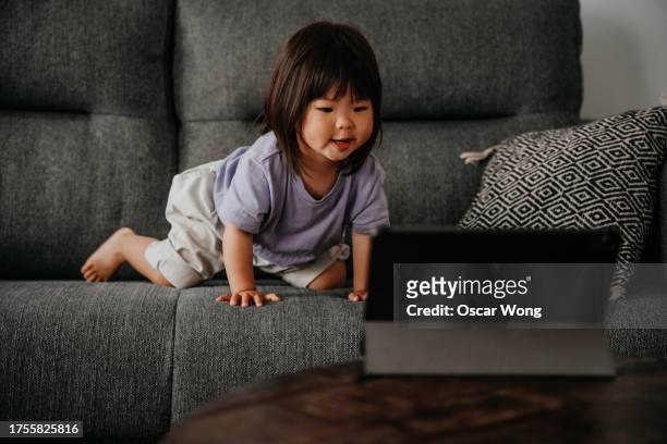cute asian toddler watching movies on digital tablet while lying on sofa - china games day 2 stock pictures, royalty-free photos & images