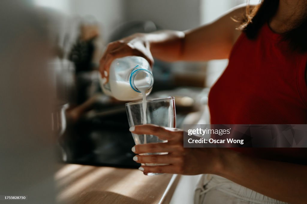 Close-up of woman pouring fresh milk from bottom to a drinking glass
