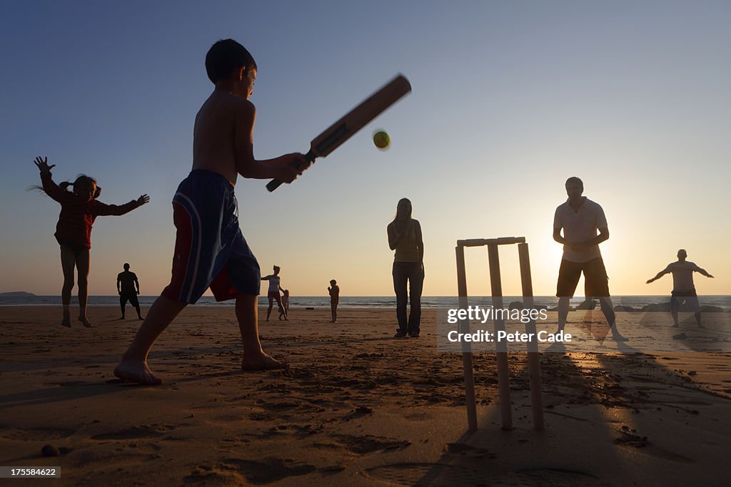 Family playing cricket on beach at sunset