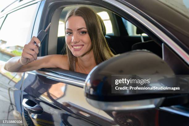 glückliche junge frau sitzt in einem auto und übernimmt nach dem gottesdienst einen schlüssel aus einem auto. - happy client by broken car stock-fotos und bilder