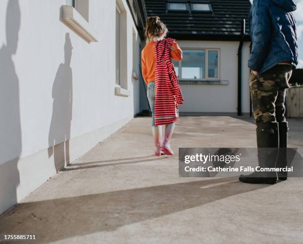 children arrive home, walking over a paved yard, casting long shadows on an exterior wall - paved yard stock-fotos und bilder