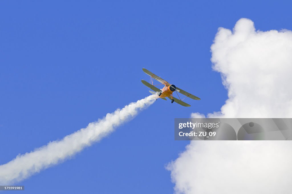 Biplane with a vapour trail, blue sky and cloud