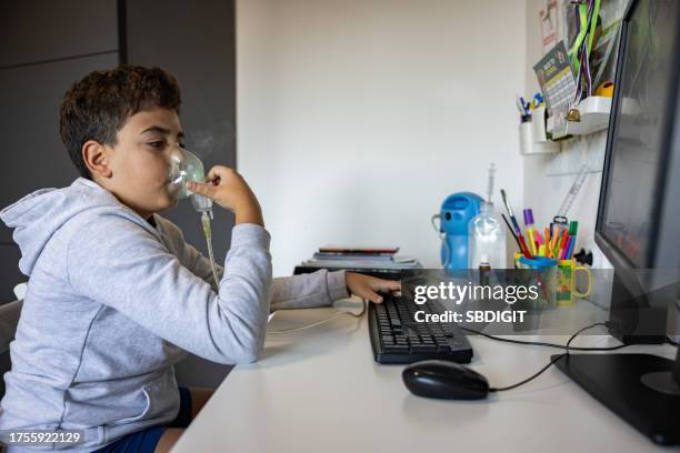 asthmatic caucasian boy using computer, while using an nebulizer for treatment - respiratory infection stock pictures, royalty-free photos & images