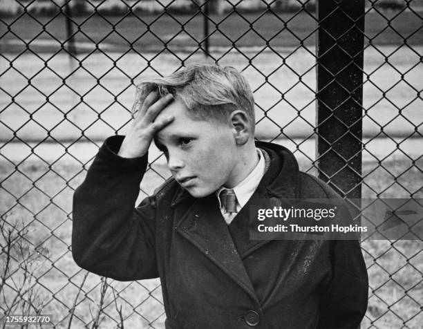 Eric Campbell, son of an engineer at the Atomic Energy Research Establishment , his left hand on his forehead as he stands before a chainlink fence...