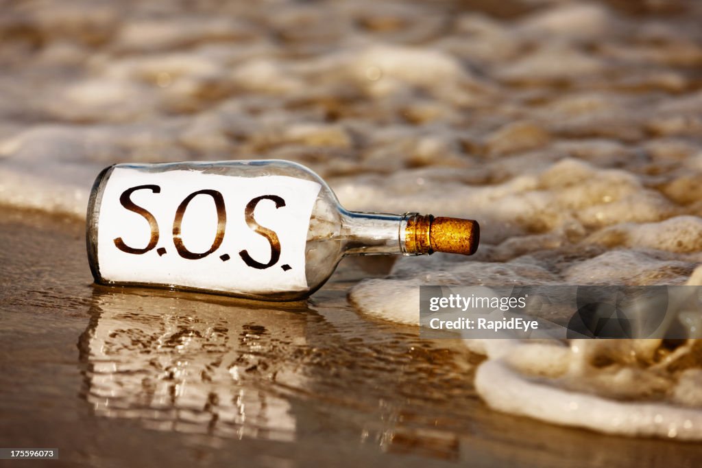 Primer plano de SOS mensaje en una botella en shoreline