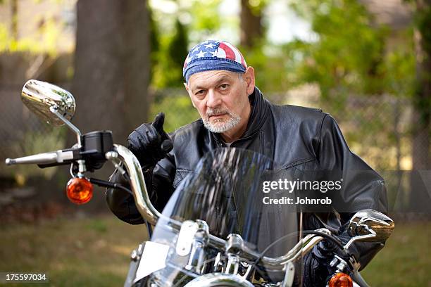 angry biker in leather jacket on motorcycle pointing toward camera - bandana stockfoto's en -beelden