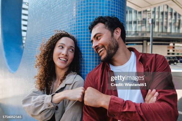 happy man and woman giving fist bump to each other near blue wall - fist bump stock pictures, royalty-free photos & images