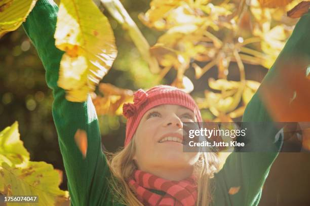 close up of a smiling young girl with her arms in the air surrounded by leaves - girl looking down stock pictures, royalty-free photos & images