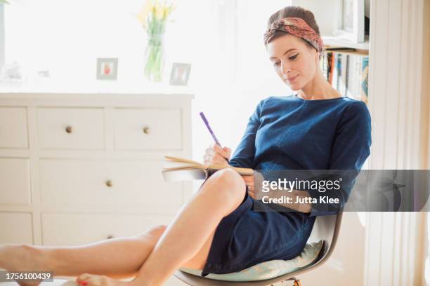 woman sitting on chair writing on notebook - girlie room stock pictures, royalty-free photos & images