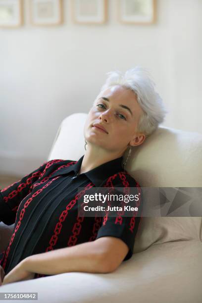 portrait of young woman sitting on armchair - platinablond haar stockfoto's en -beelden