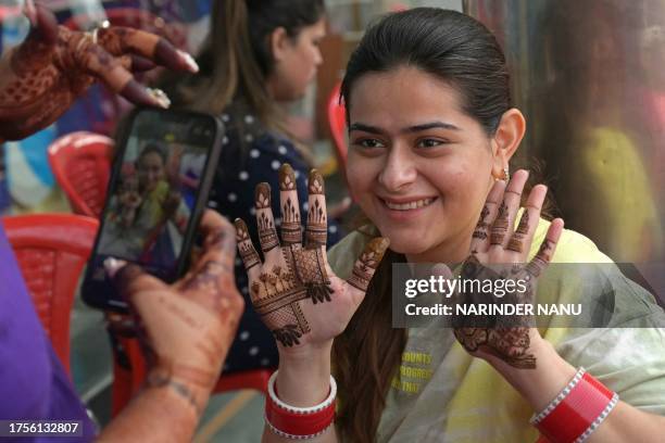 Woman poses for picture after getting her hands decorated with henna on the eve of the Hindu festival of Karva Chauth, in which married women fast...