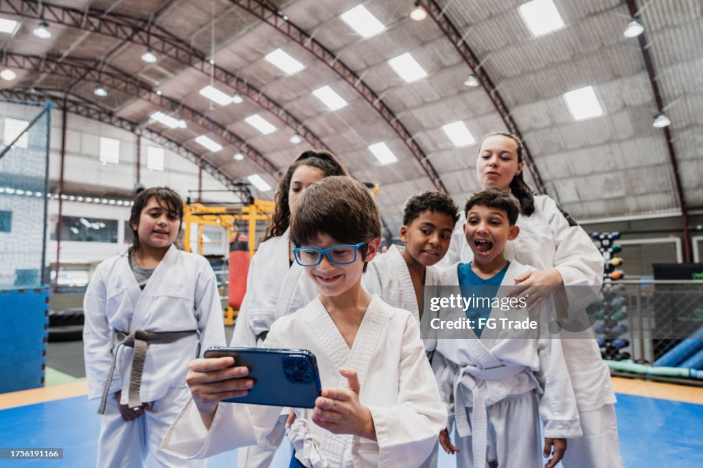 Boy taking selfies on the mobile phone with friends and sensei in a judo class at the gym
