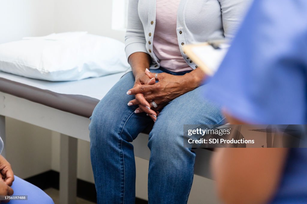 Unrecognizable senior woman clasps hands during discussion with medical personnel