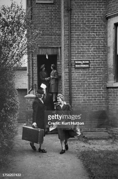 Two women, both carrying bags and suitcases, leaving the National Institute of House Workers, two women seen in the doorway in the background, in...