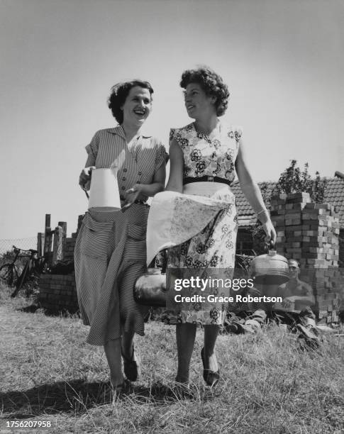 Two women, one holding a jug while the other holds a kettle, a stack of bricks oin the background, on a self-build housing development in Ipswich,...