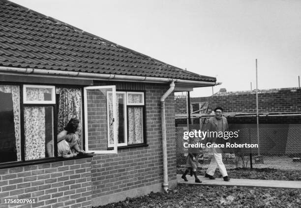 Mother and son lean out from a window of their bungalow home as the father and daughter leave the self-built property in Ipswich, Suffolk, England,...