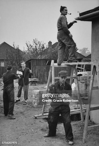 Group of men, one carrying bricks and one standing on a platform supported on trestles on a self-build housing development in Ipswich, Suffolk,...