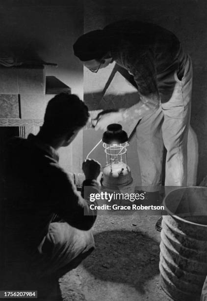 Man plastering a wall as a second man holds a camping light at a self-build housing development in Ipswich, Suffolk, England, 1955. Original...