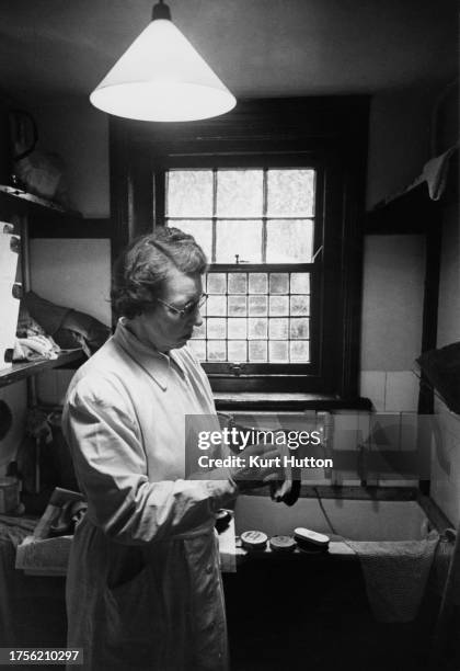 Woman holding a shoe and shoebrush as she cleans shoes, tins of polish and another brush on the edge of a sink in the background, at the National...