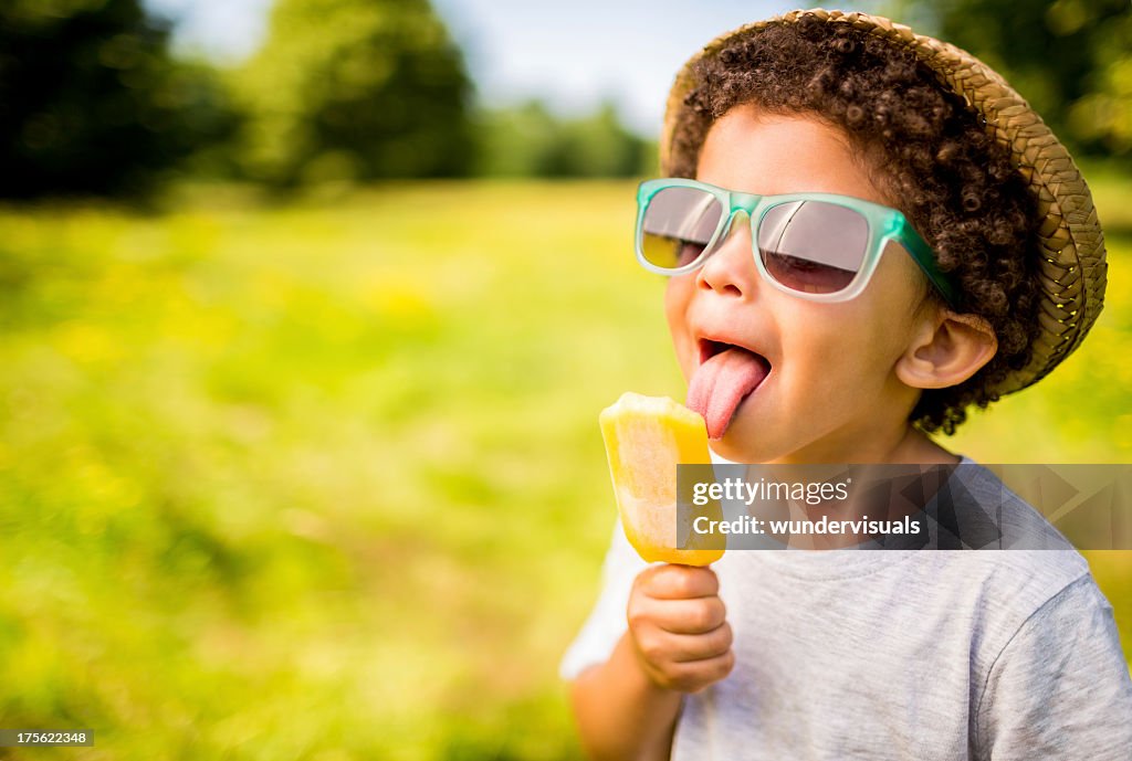 Niño en gafas de sol y sombrero comer popsicle al aire libre