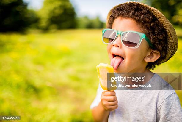 niño en gafas de sol y sombrero comer popsicle al aire libre - confectionery fotografías e imágenes de stock