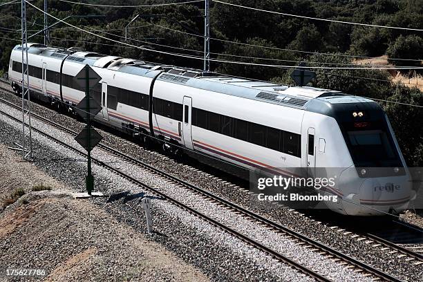Train operated by Renfe Operadora SC travels beneath overhead power lines near El Escorial, in northern Madrid, Spain, on Sunday, Aug. 4, 2013....