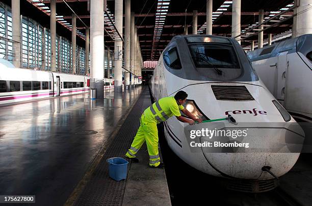 Worker cleans the front of an Alta Velocidad Espanola high-speed train operated by Renfe Operadora SC as it sits at a platform at Atocha train...