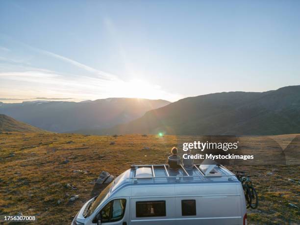 concetto di viaggio su strada girato con drone - coppia sul tetto di un camper che guarda il tramonto, autunno - camper foto e immagini stock