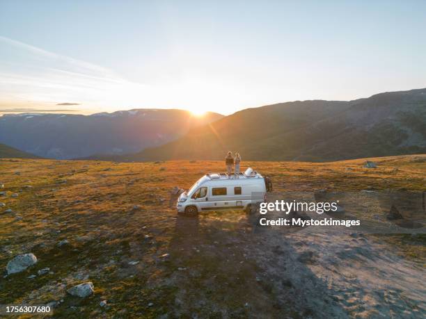 drohnenaufnahme roadtrip-konzept - paar auf dem dach eines wohnmobils beobachtet sonnenuntergang, herbst - lieferwagen stock-fotos und bilder