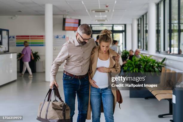 pregnant woman in labour waiting to be admitted to hospital. future mother having painful contractions, walking with husband to labour and delivery reception to check in. - muskelkontraktion stock-fotos und bilder