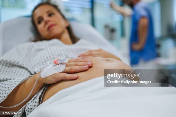 pregnant woman in labour waiting for examination in maternity ward. woman during early stage of childbirth at the hospital holding her belly, feeling painful contractions. - labor childbirth stock pictures, royalty-free photos & images