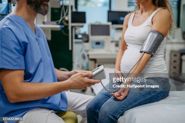 obstetrician gynaecologist measuring pregnant woman's blood pressure as a part of prenatal care, visit. pregnant woman on pregnancy check-up in doctor’s office. preeclampsia and risk of pregnancy complications with high blood pressure. - baby in the womb stock pictures, royalty-free photos & images