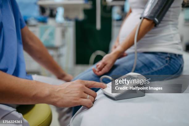 obstetrician gynaecologist measuring pregnant woman's blood pressure as a part of prenatal care, visit. pregnant woman on pregnancy check-up in doctor’s office. preeclampsia and risk of pregnancy complications with high blood pressure. - high blood pressure stockfoto's en -beelden