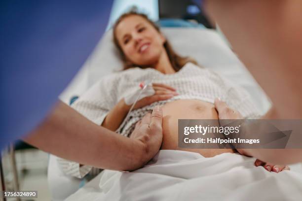 obstetrician examining pregnant woman in hospital, touching woman’s belly, examine position of baby, breach position, size of baby and movements. woman in labour laying on hospital bed, talking with ob-gyn doctor in maternity ward. - comadrona fotografías e imágenes de stock