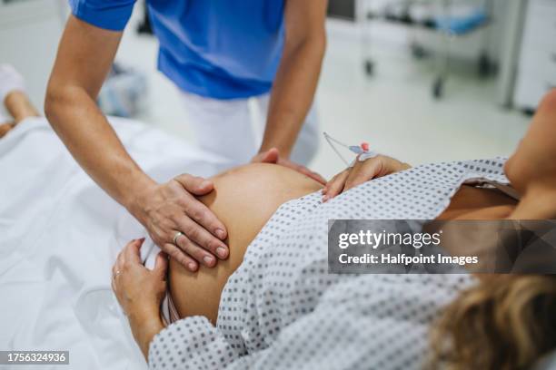 obstetrician examining pregnant woman in hospital, touching woman’s belly, examine position of baby, breach position, size of baby and movements. woman in labour laying on hospital bed, talking with ob-gyn doctor in maternity ward. - doctor's surgery stock pictures, royalty-free photos & images
