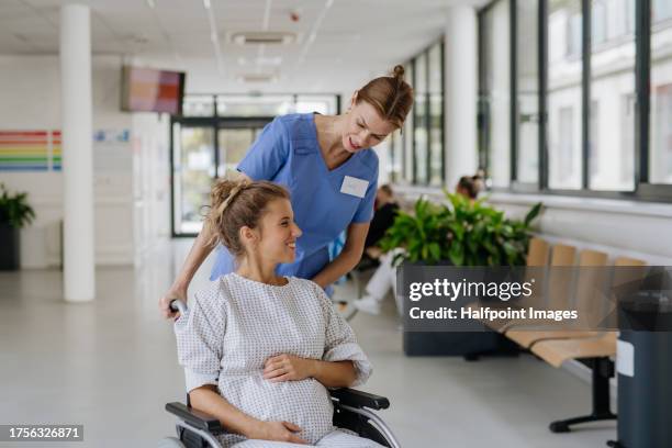 nurse pushing pregnant woman on wheelchair in hospital. woman in labor, dressed in hospital gown talking with midwife. woman giving birth at the maternity hospital, ward. - comadrona fotografías e imágenes de stock