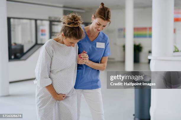 nurse helping pregnant woman with painful labour contractions in the hospital hall. woman in labor, dressed in hospital gown doing breathing exercises, deep breathing to relieve pain. - comadrona fotografías e imágenes de stock